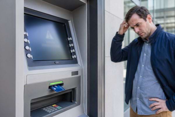 un homme qui se gratte la t&ecirc;te devant un distributeur d'argent