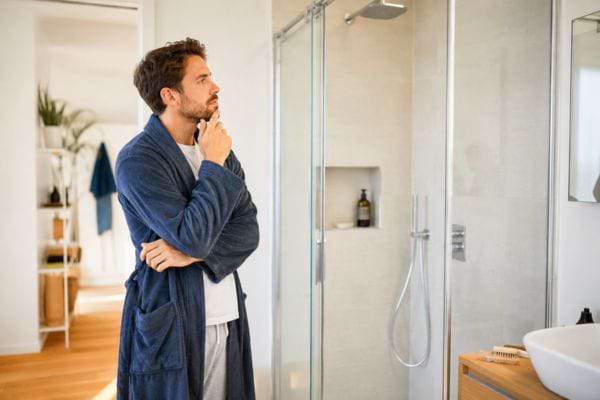 Homme pensif en peignoir devant sa douche.