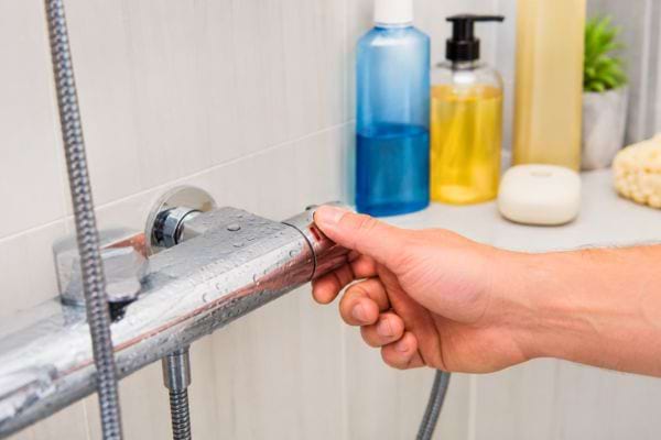 Main r&eacute;glant le robinet d&rsquo;une douche moderne.