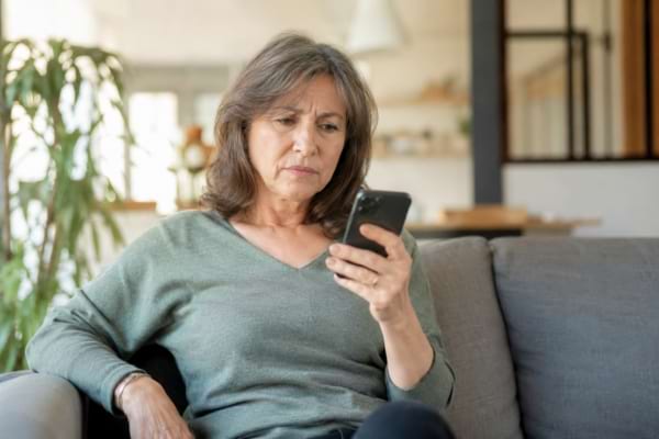 une personne d'âge mûr assise dans son salon, regardant l'écran de son smartphone