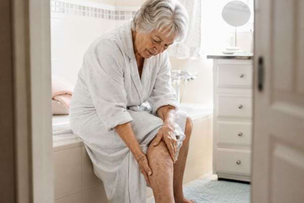 Femme senior touchant sa jambe dans une salle de bain.