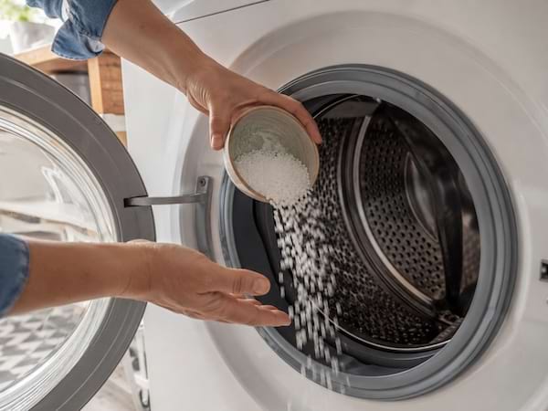 Des mains versent du gros sel dans le tambour d’une machine à laver