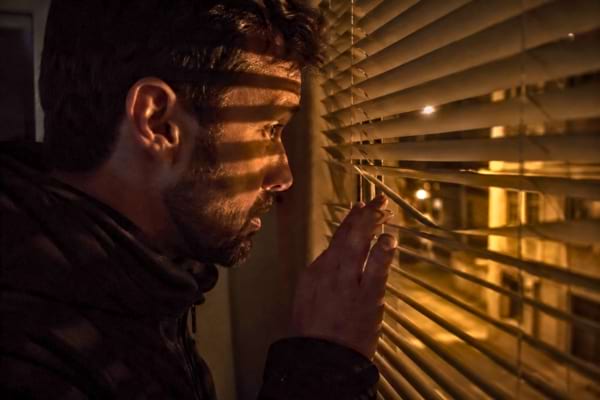 La silhouette sombre d'une personne regardant anxieusement &agrave; travers les stores d'une fen&ecirc;tre la nuit
