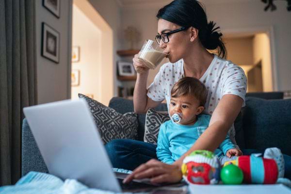 une maman boit dans une tasse avec un b&eacute;b&eacute; devant un ordinateur