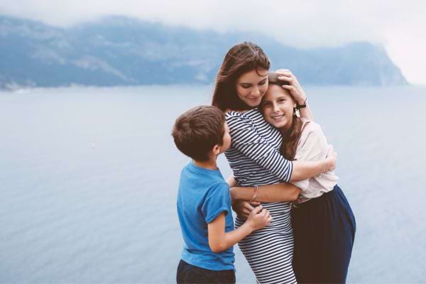 une m&egrave;re enlace un gar&ccedil;on et une fille devant un lac
