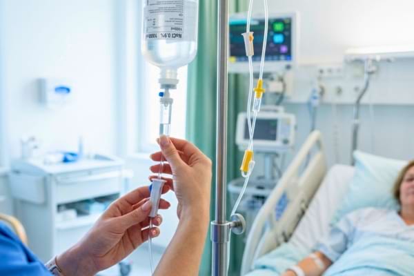 mains attentionn&eacute;es d'une infirmi&egrave;re ajustant un goutte-&agrave;-goutte intraveineux pr&egrave;s d'un lit d'h&ocirc;pital