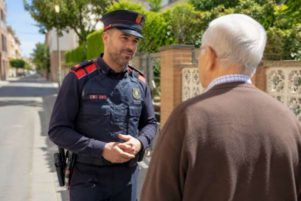 Un policier espagnol (Mossos d'Esquadra) en uniforme discutant calmement avec une personne âgée
