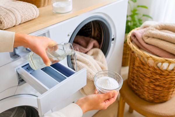Main versant du vinaigre dans le bac de la machine &agrave; laver