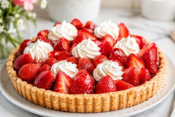 Tarte aux fraises maison garnie de fraises rouges brillantes et de rosaces de chantilly