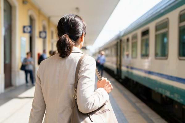 Femme de dos marchant sur un quai de gare vers un train pr&ecirc;t au d&eacute;part