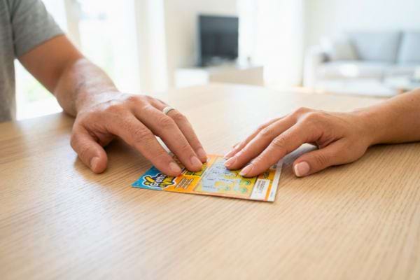 Deux personnes posant leurs mains sur un ticket &agrave; gratter sur une table
