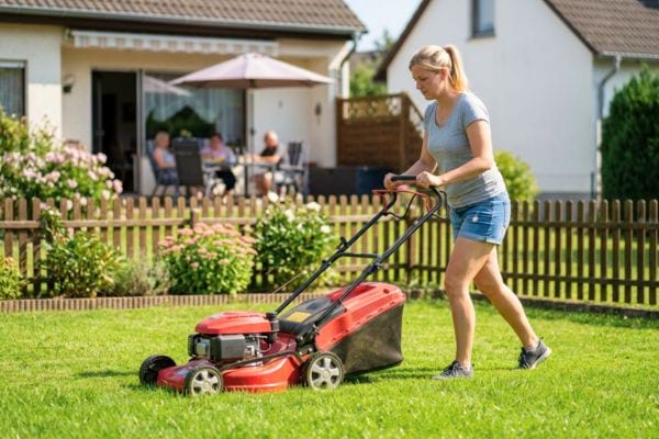 Femme passant la tondeuse dans un jardin devant une maison