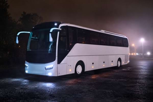 un grand bus touristique blanc et moderne stationn&eacute; dans une zone sombre et isol&eacute;e