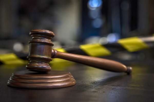 Un marteau de juge en bois pos&eacute; sur un bureau sombre.
