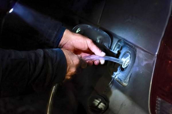 mains d'une pPersonne ins&eacute;rant un tuyau transparent dans une trappe m&eacute;tallique sur le flanc d'un v&eacute;hicule