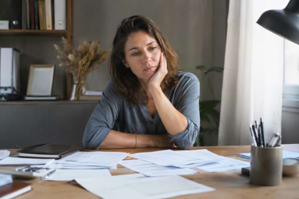 une femme l'air fatiguée et pensive, assise à un bureau avec des papiers.
