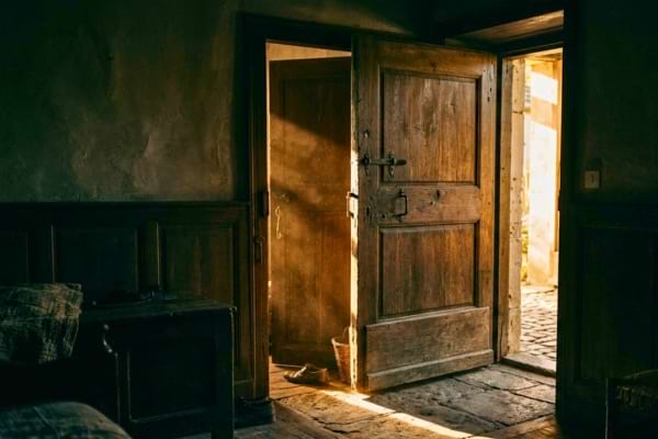 ne porte en bois entrouverte laissant passer un fin rayon de lumi&egrave;re dor&eacute;e dans une pi&egrave;ce sombre