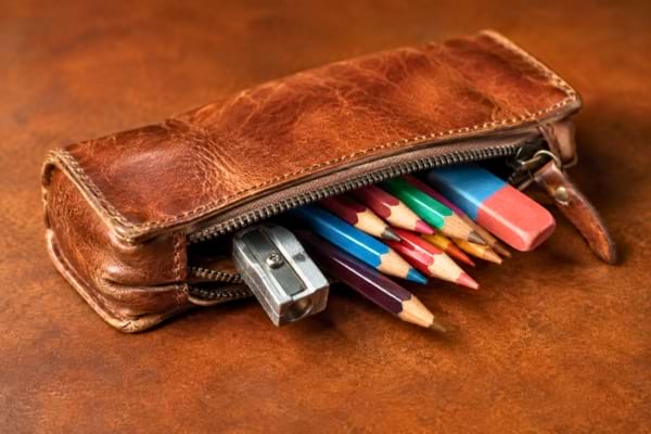 Une trousse d'&eacute;colier en cuir vintage entrouverte, laissant d&eacute;passer des crayons de couleur,