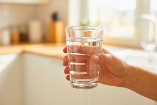 Main tenant un verre d’eau dans une cuisine lumineuse