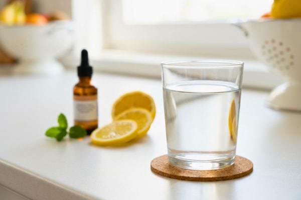 Verre d’eau posé avec citron et flacon sur un plan de travail