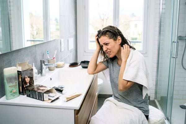 femme brune qui fait une allergie après une coloration de cheveux dans sa salle de bain