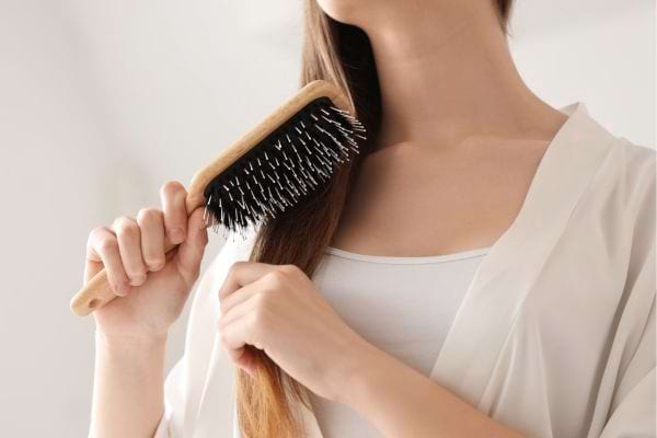 femme qui brosse ses cheveux longs avec une brosse en bois