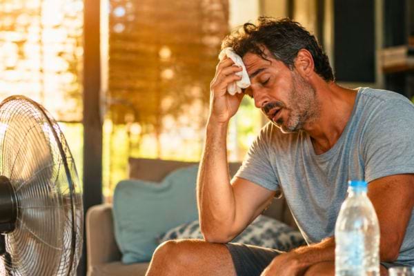 Homme &eacute;puis&eacute; par la chaleur devant un ventilateur avec une bouteille d&rsquo;eau