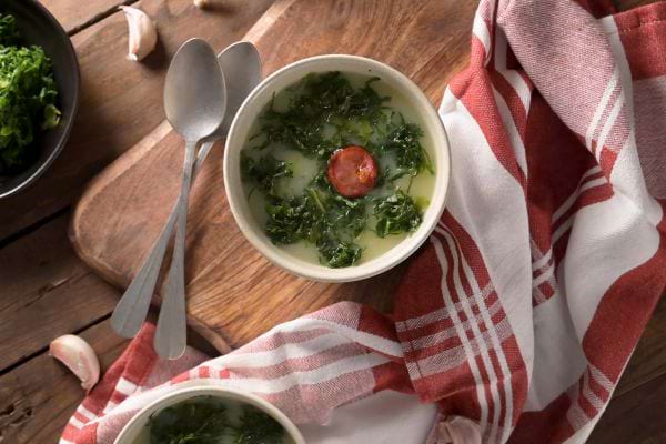 un bol de caldi verde avec du chorizo à côté d'un torchon rouge et blanc