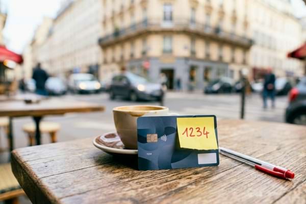 une carte bancaire pos&eacute;e sur une table de caf&eacute; en bois, avec un petit post-it jaune coll&eacute; dessus