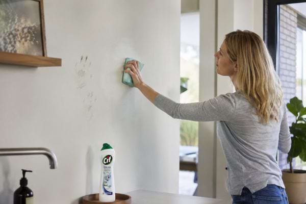 Personne nettoyant des traces sur un mur lavable avec du Cif dans une cuisine.