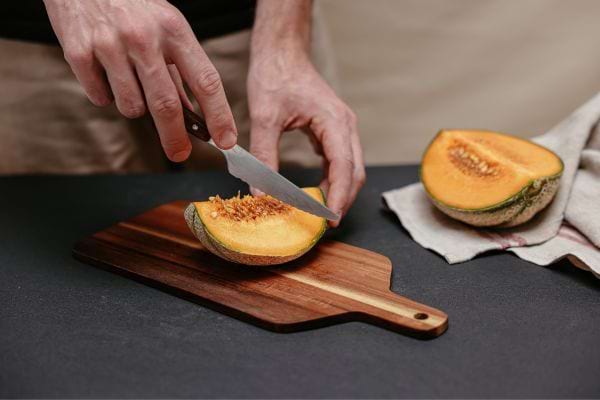 Couteau coupant un melon entier sur une planche en bois