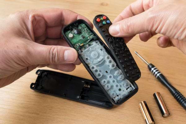 Télécommande démontée avec piles retirées, tournevis et composants internes visibles