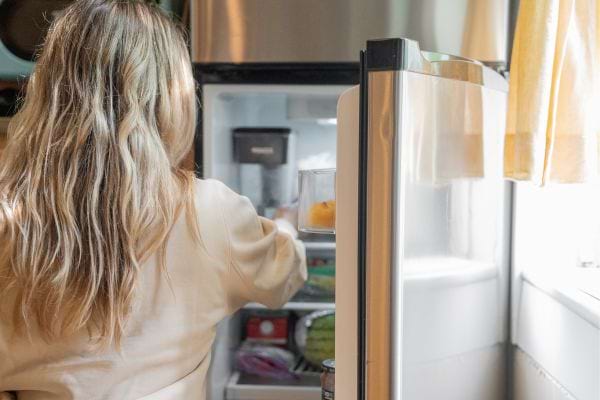 une femme est devant un frigo ouvert et prend quelque chose