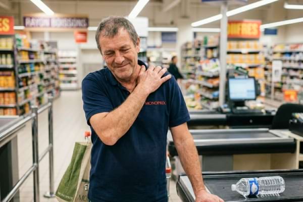 un caissier de supermarch&eacute; se massant l'&eacute;paule ou le poignet avec une expression de douleur l&eacute;g&egrave;re.