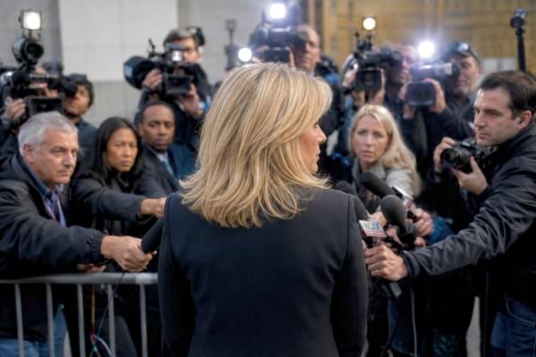 une femme de dos face à une foule de journalistes avec des micros tendus
