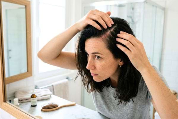 femme brune qui regarde son cuir chevelu dans un miroir