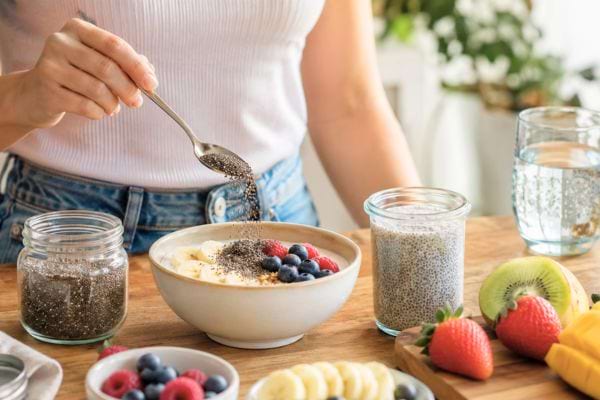 Personne ajoutant une cuillère de graines de chia dans un bol de fruits et yaourt.