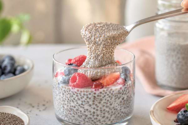 Cuillère soulevant un pudding de chia gélifié avec fruits rouges et myrtilles.