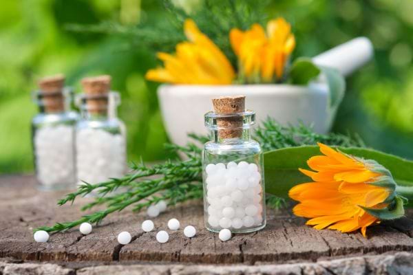 3 bouteilles en verre de granules d'homéopathie sur un support en bois avec des fleurs oranges