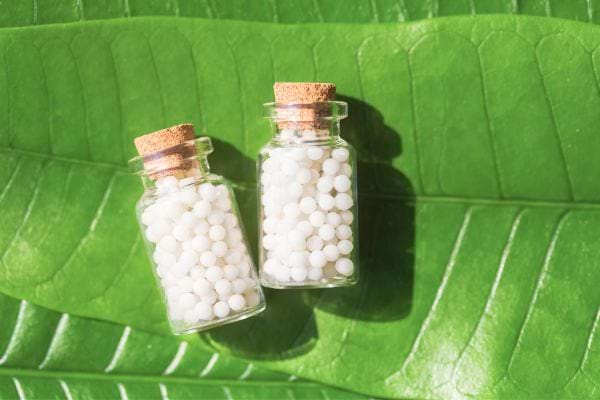 deux bouteilles en verre de granules d'homéopathie déposées sur des feuilles vertes