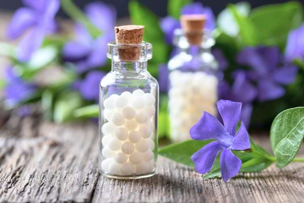 2 bouteilles en verre de granules d'homéopathie sur un support en bois avec des fleurs bleues