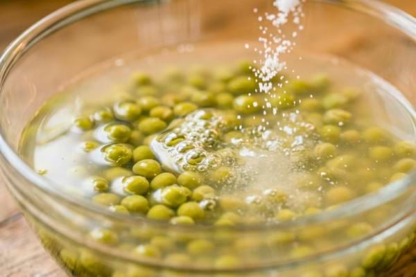 un bol en verre transparent rempli de petits pois en conserve et de leur liquide trouble