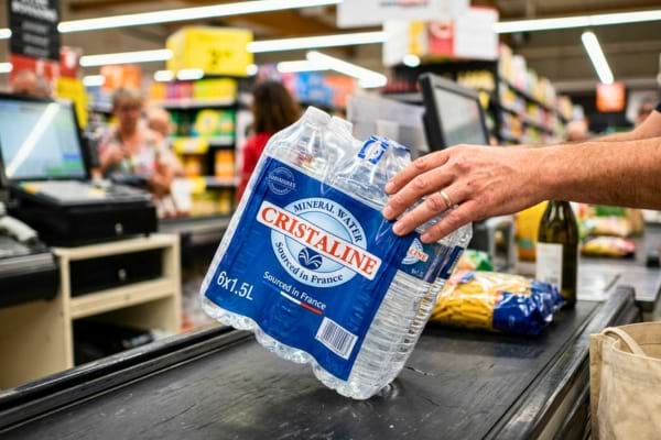 un pack d'eau min&eacute;rale lourd pos&eacute; sur un tapis roulant noir de supermarch&eacute;.