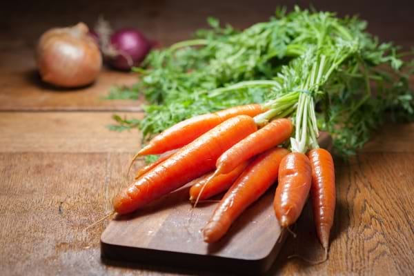 des carottes avec leurs f&acirc;nes sur une planche &agrave; d&eacute;couper avec des oignons rouges et jaunes