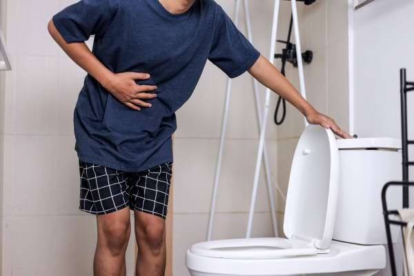 un homme en cale&ccedil;on se tient le ventre pr&egrave;s des toilettes
