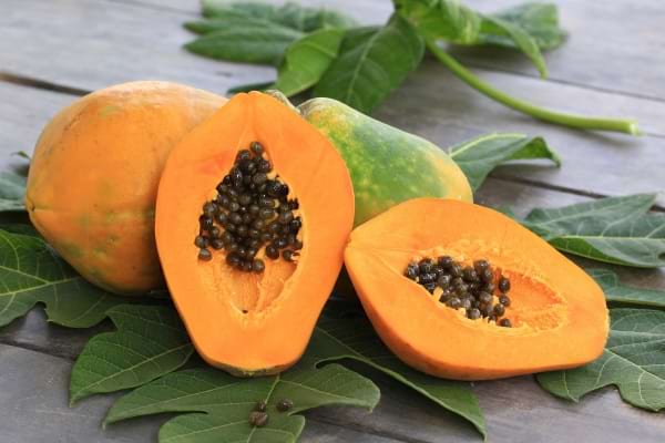 une papaye coup&eacute;e en deux et une papaye enti&egrave;re sur des feuilles