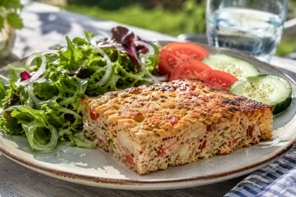 Part de flan au thon servie avec salade verte, tomates et rondelles de concombre.