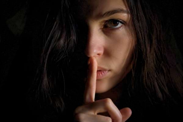 un visage de femme dans l'ombre avec un doigt sur la bouche pour faire le signe