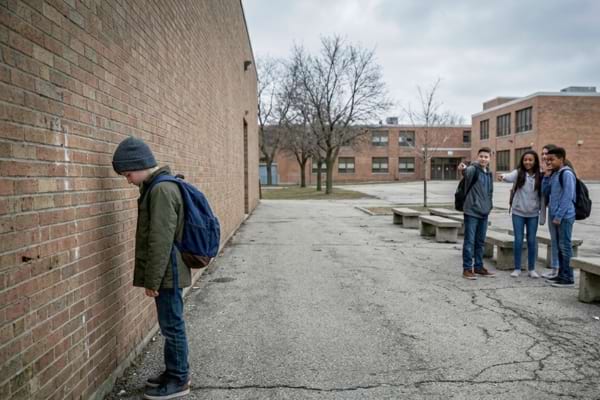 Un jeune élève portant un bonnet se tient seul et isolé près d'un mur