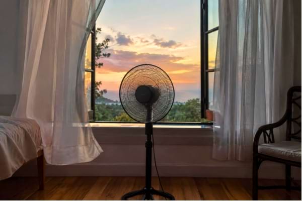 un ventilateur sur pied pos&eacute; face &agrave; une fen&ecirc;tre grande ouverte, vue de l'int&eacute;rieur vers l'ext&eacute;rieur